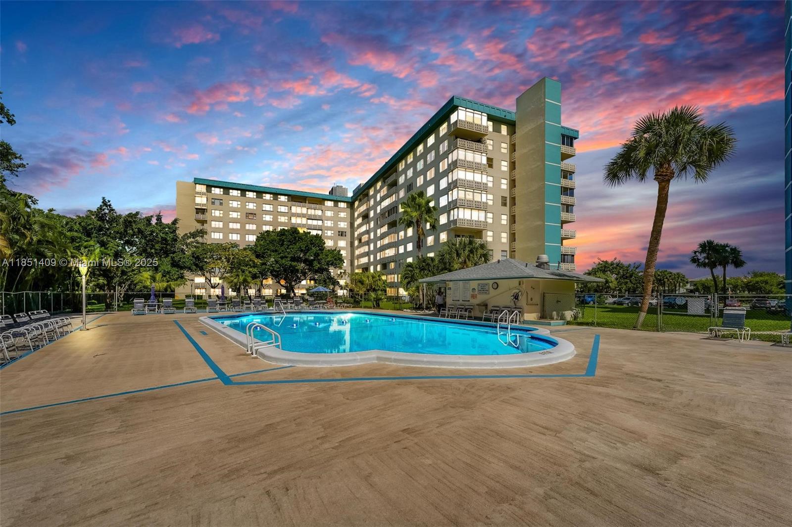 An outdoor swimming pool sits in front of a multi-story apartment building at sunset — 4330 Hillcrest Dr # 516, Hollywood FL 33021, HOLLYWOOD, FL