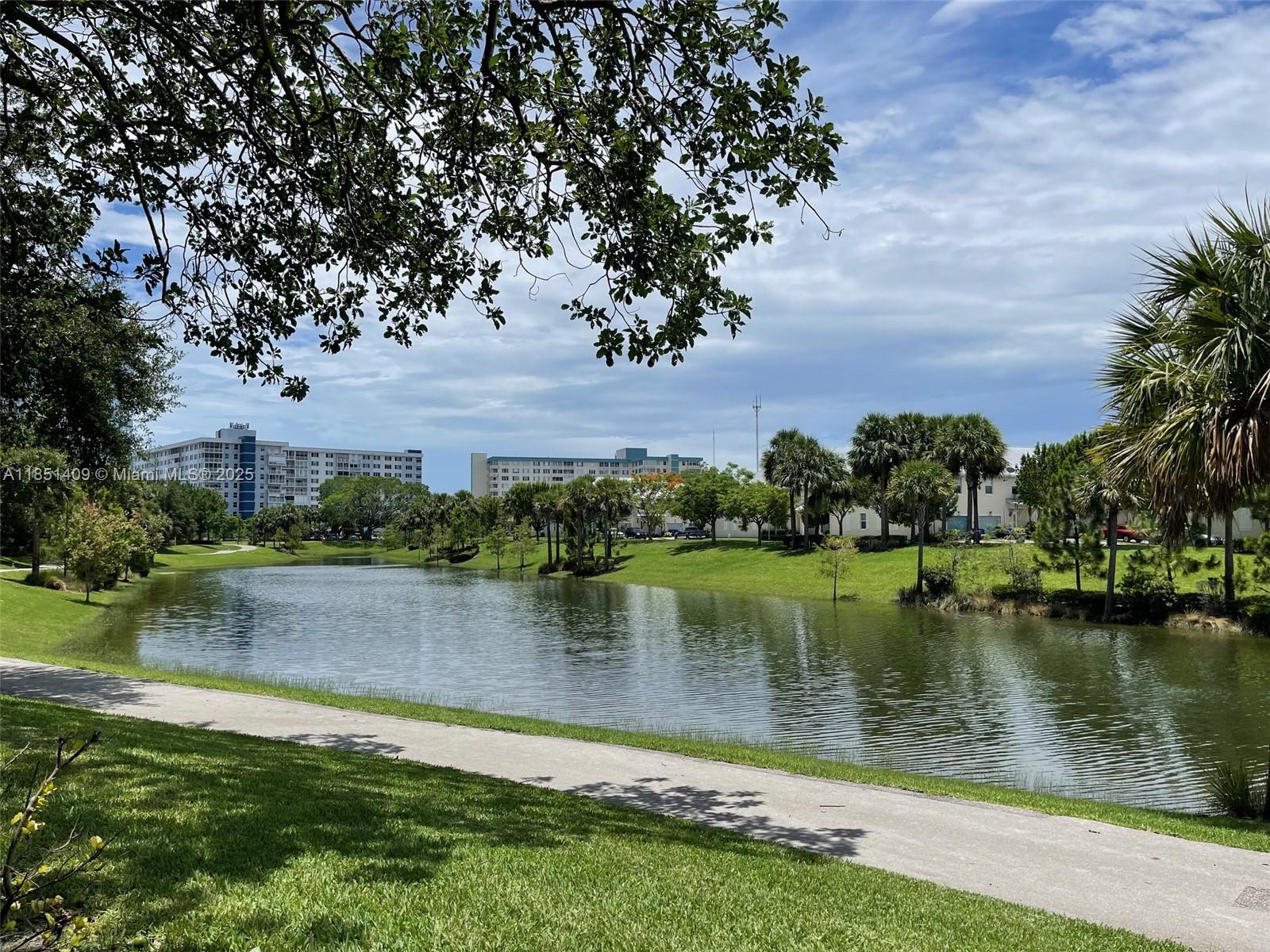 A paved walking path winds alongside a pond surrounded by green lawns and palm trees — 4330 Hillcrest Dr # 516, Hollywood FL 33021, HOLLYWOOD, FL