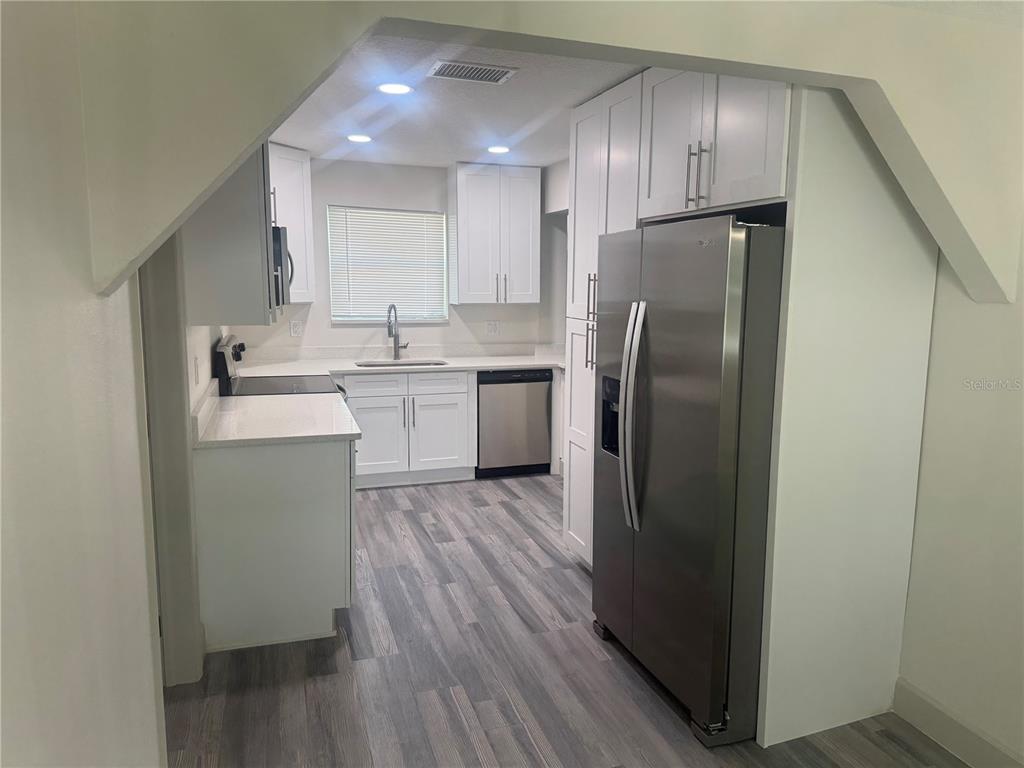 A modern kitchen features white cabinets, stainless steel appliances, and gray wood-look flooring — 1149 LA SALLE STREET, CLEARWATER, FL