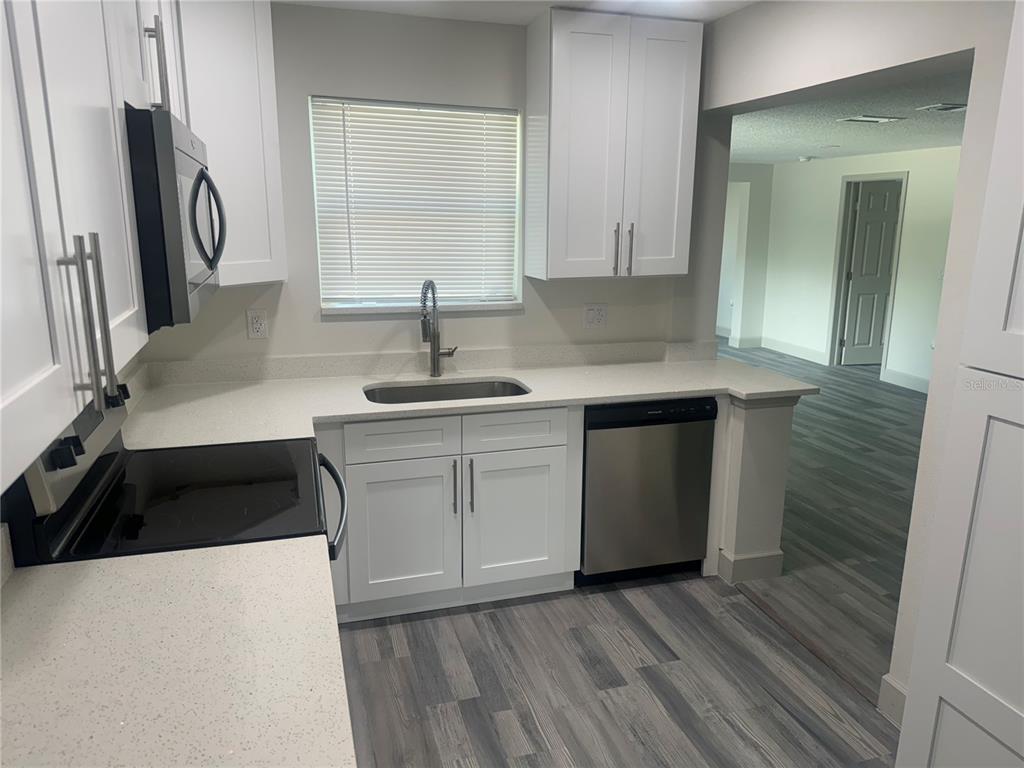 A kitchen features white cabinets, light countertops, stainless steel appliances, and gray wood-look flooring — 1149 LA SALLE STREET, CLEARWATER, FL