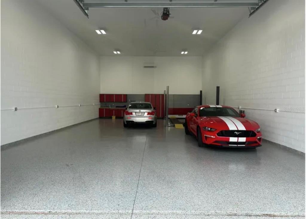 A spacious garage with a speckled epoxy floor, white block walls, and two parked cars — 144 ANCHOR ROAD UNIT B-9, ROTONDA WEST, FL