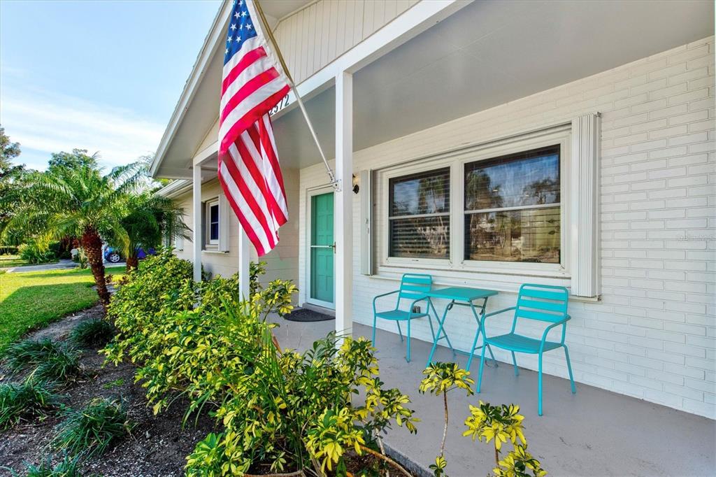 A white brick house exterior features a covered porch with two turquoise chairs and table — 2572 JEFFERSON CIRCLE, SARASOTA, FL
