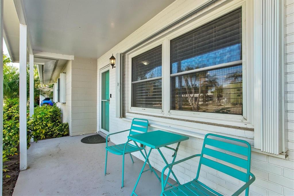 A covered porch features white brick walls, a teal door, and two matching teal chairs — 2572 JEFFERSON CIRCLE, SARASOTA, FL