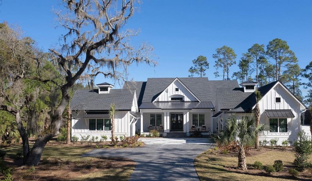 A white farmhouse-style home with a dark roof and a paved driveway sits among trees — 4299 ROYAL SKY COURT, BROOKSVILLE, FL