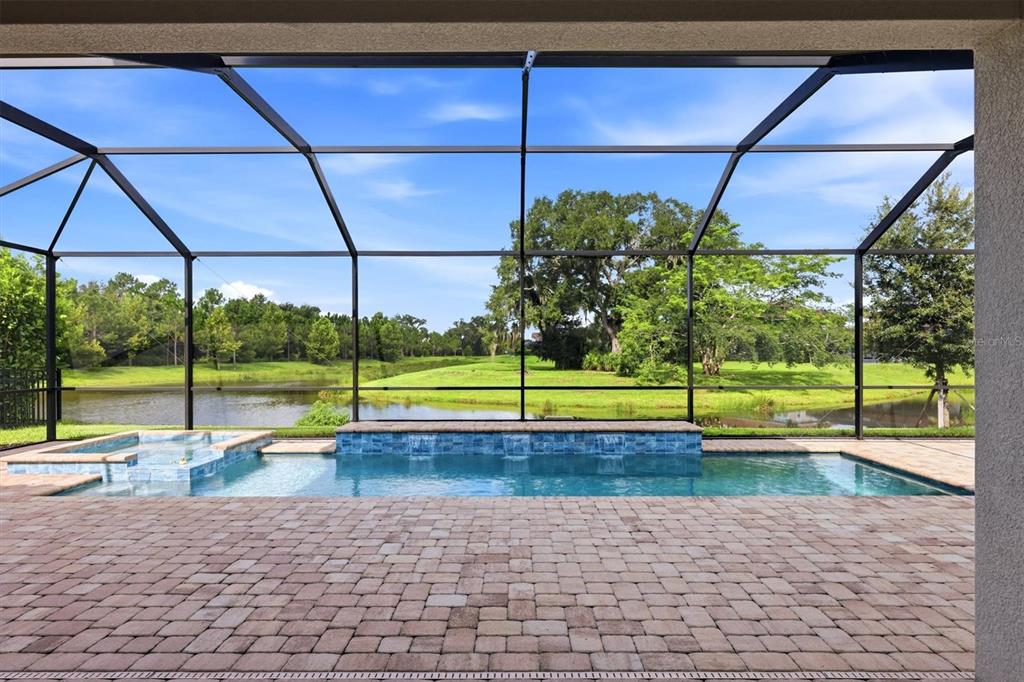 A screened-in patio features a paver deck, a swimming pool with a spa, and water views — 7271 GREAT EGRET BOULEVARD, SARASOTA, FL
