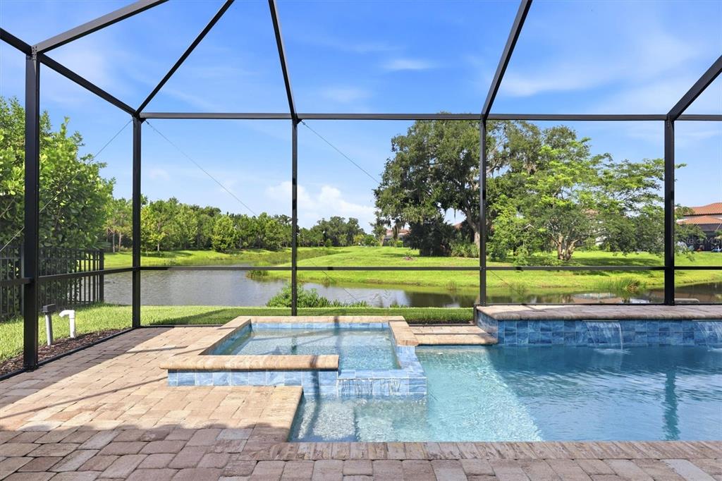 A screened-in pool and spa area overlooking a pond and grassy landscape — 7271 GREAT EGRET BOULEVARD, SARASOTA, FL