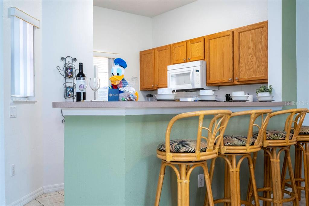 A kitchen features wooden cabinets, a microwave, and a breakfast bar with three rattan stools — 1065 PARK RIDGE CIRCLE, KISSIMMEE, FL