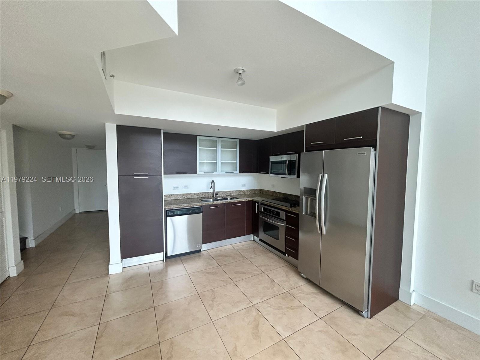 A kitchen features dark brown cabinets, stainless steel appliances, granite countertops, and light tile flooring — 41 SE 5th St # 907, Miami FL 33131, MIAMI, FL