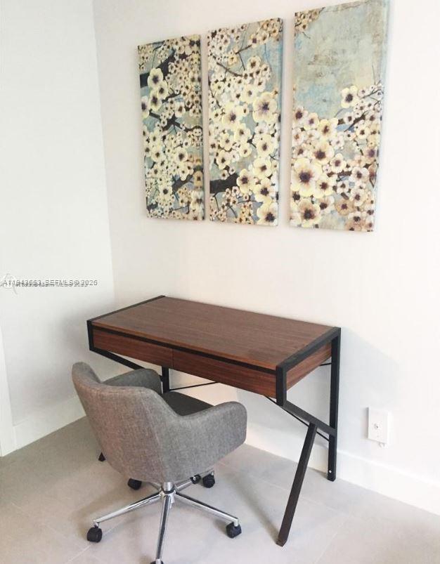 A home office space features a wooden desk, a gray chair, and floral wall art — 100 Lincoln Rd # 426, Miami Beach FL 33139, MIAMI BEACH, FL