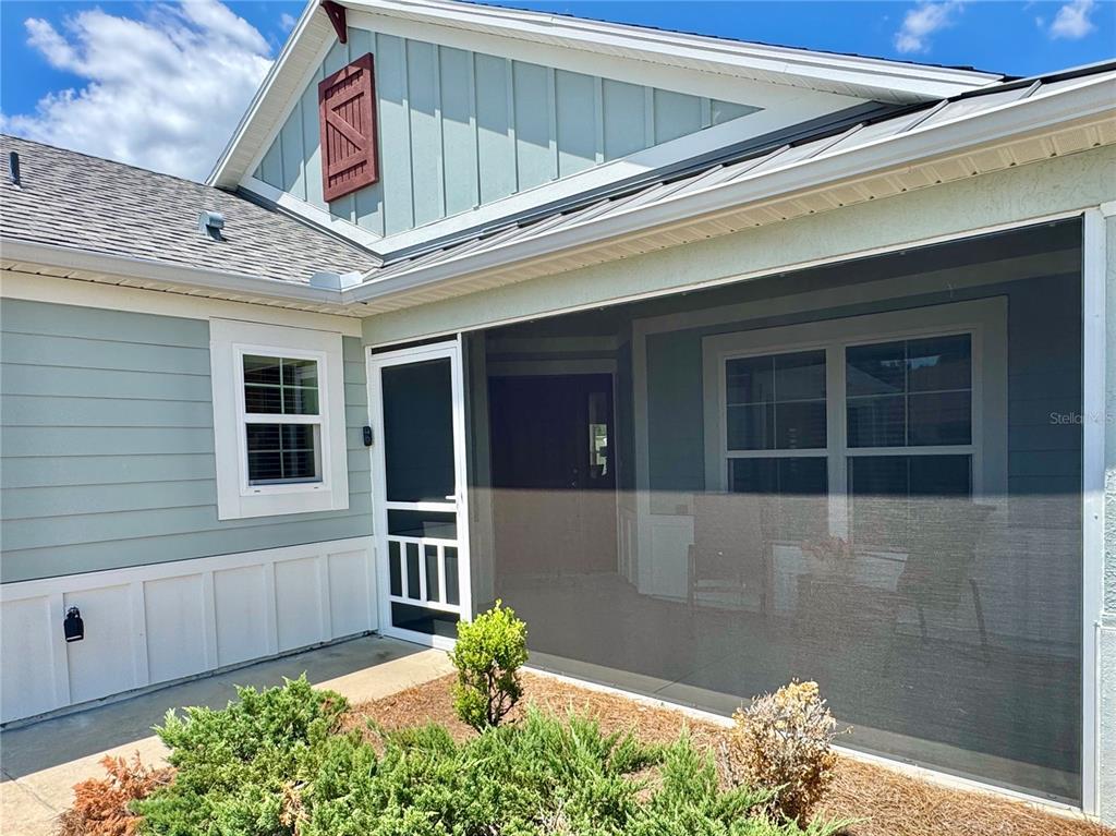 A screened-in porch entrance features light green siding, a white door, and a decorative shutter — 2931 CHARLEVOIX STREET, THE VILLAGES, FL