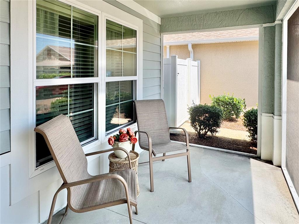 A covered patio features two chairs, a small side table with flowers, and a screen enclosure — 2931 CHARLEVOIX STREET, THE VILLAGES, FL
