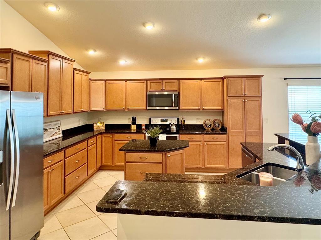A kitchen features wood cabinets, dark granite countertops, stainless steel appliances, and tile flooring — 2931 CHARLEVOIX STREET, THE VILLAGES, FL
