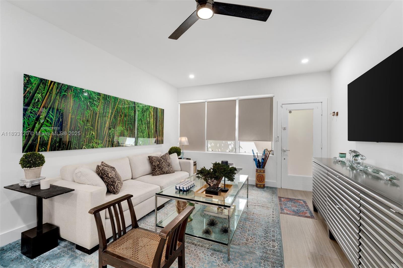 A modern living room features a white sofa, glass coffee table, and large bamboo wall art — 4720 Pine Tree Drive # 2, Miami Beach FL 33140, MIAMI BEACH, FL