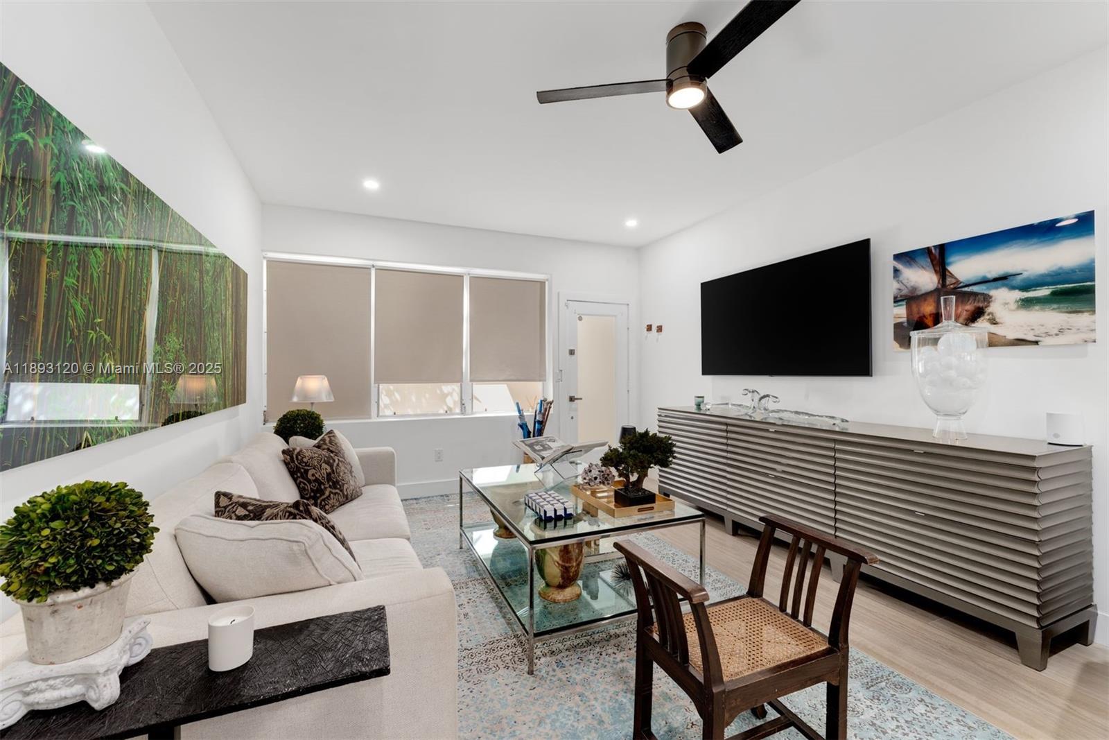 A living room features a white sofa, glass coffee table, wall-mounted television, and ceiling fan — 4720 Pine Tree Drive # 2, Miami Beach FL 33140, MIAMI BEACH, FL