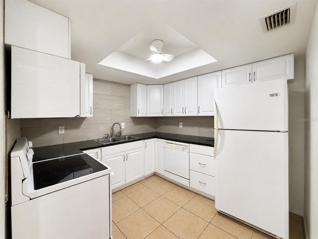 A kitchen features white cabinets, black countertops, a white refrigerator, and tan tile flooring — 568 BAHIA CIRCLE UNIT B, OCALA, FL