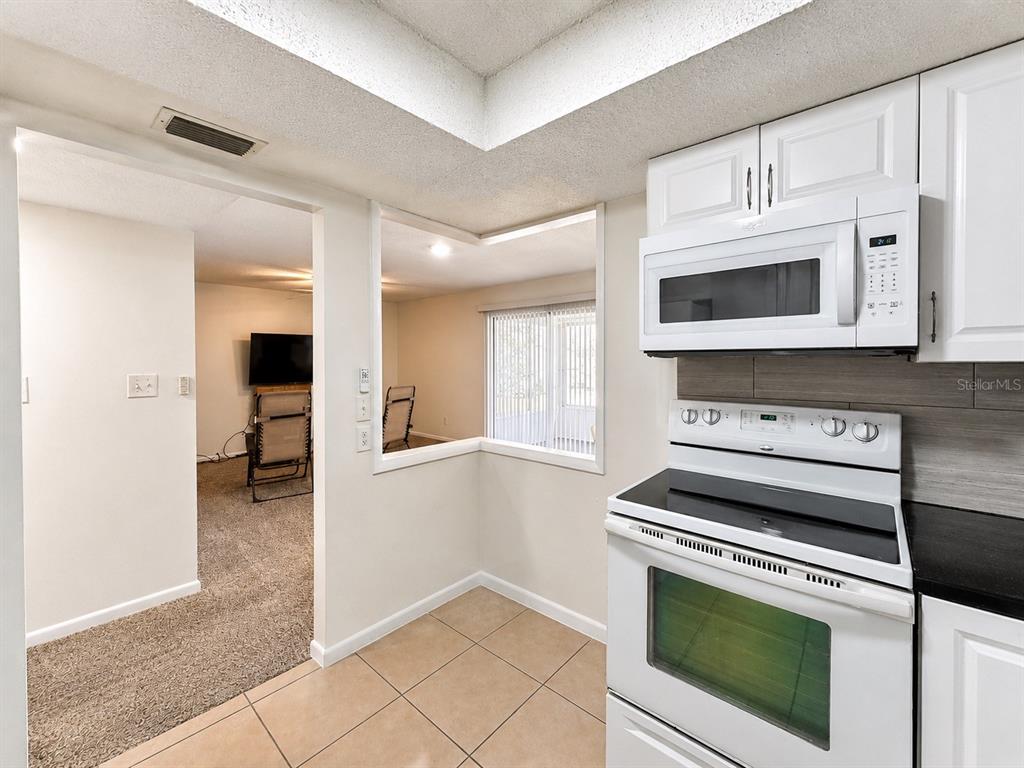 A kitchen with white appliances and cabinets overlooks a carpeted living area through a cutout — 568 BAHIA CIRCLE UNIT B, OCALA, FL
