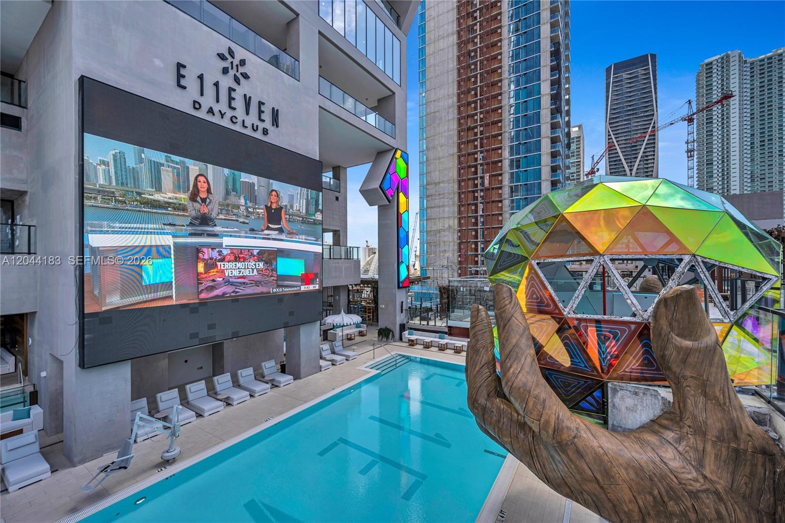 An outdoor pool area at E11EVEN Dayclub features a large screen, lounge chairs, and sculpture — 20 NE 11th, Miami FL 33132, MIAMI, FL