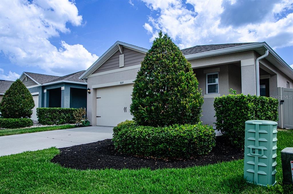 A single-story suburban house with a two-car garage, manicured landscaping, and a green utility box — 864 GUNNISON DRIVE, ORANGE CITY, FL