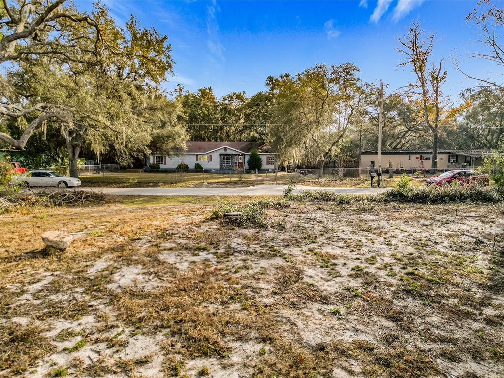 A vacant, sandy lot sits in the foreground with houses visible across a paved road — 202 NE 72ND TERRACE, OCALA, FL