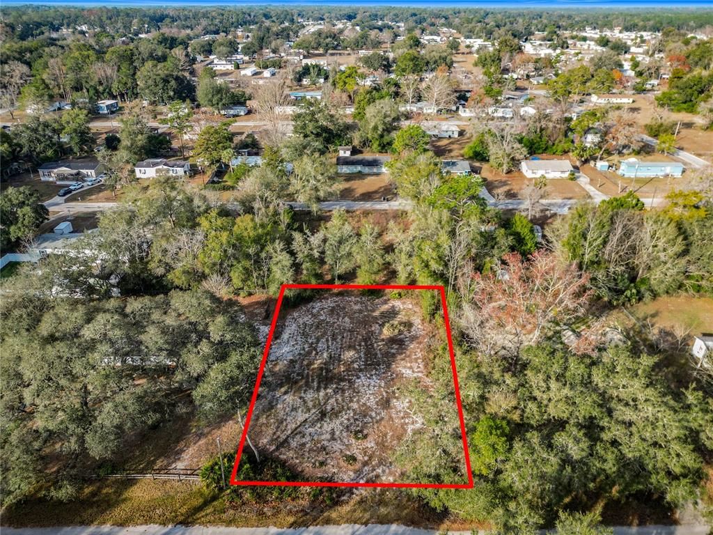 An aerial view shows a rectangular, cleared vacant lot outlined in red amidst wooded surroundings — 202 NE 72ND TERRACE, OCALA, FL