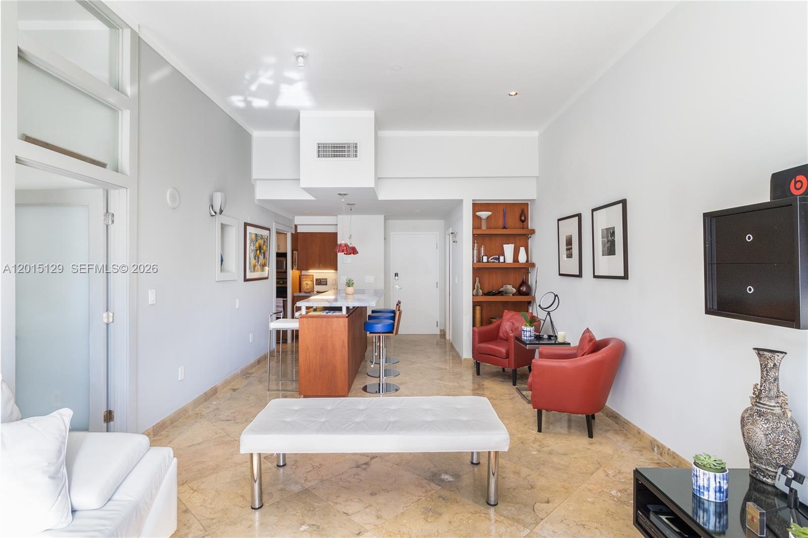 A living room features a kitchen island, red armchairs, and a white bench on tile floors — 6917 Collins Ave # 103, Miami Beach FL 33141, MIAMI BEACH, FL