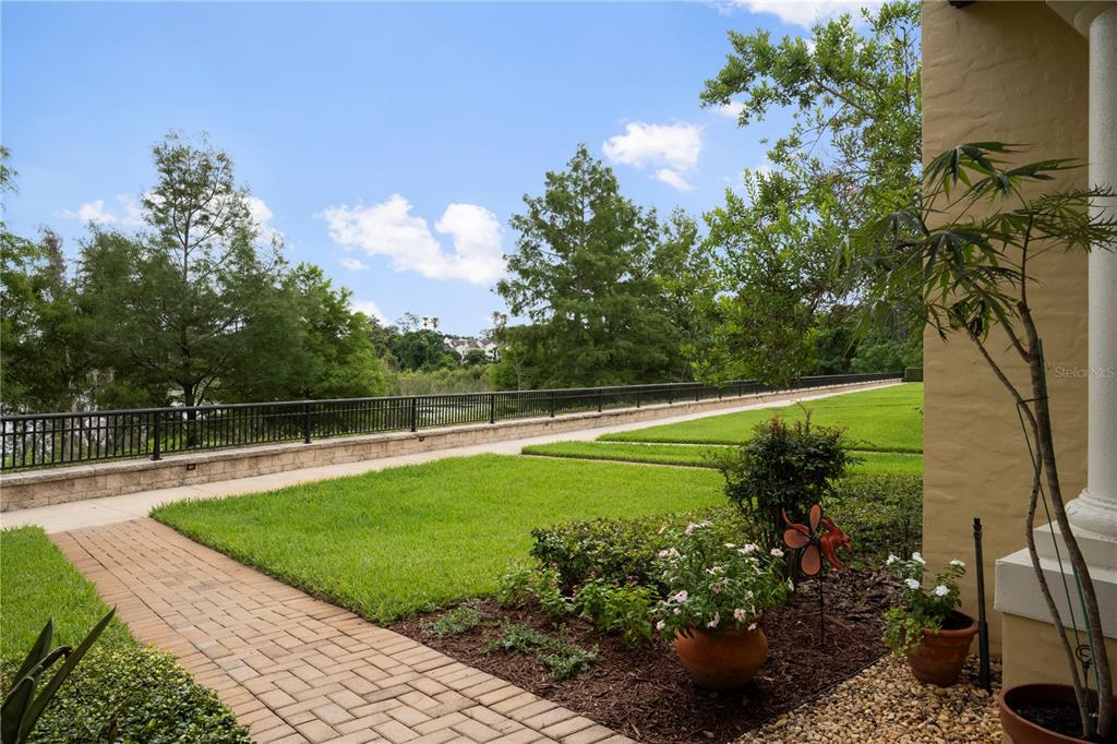 A paved walkway leads to a grassy lawn overlooking a lake with a black fence — 1132 CHARMING STREET, MAITLAND, FL