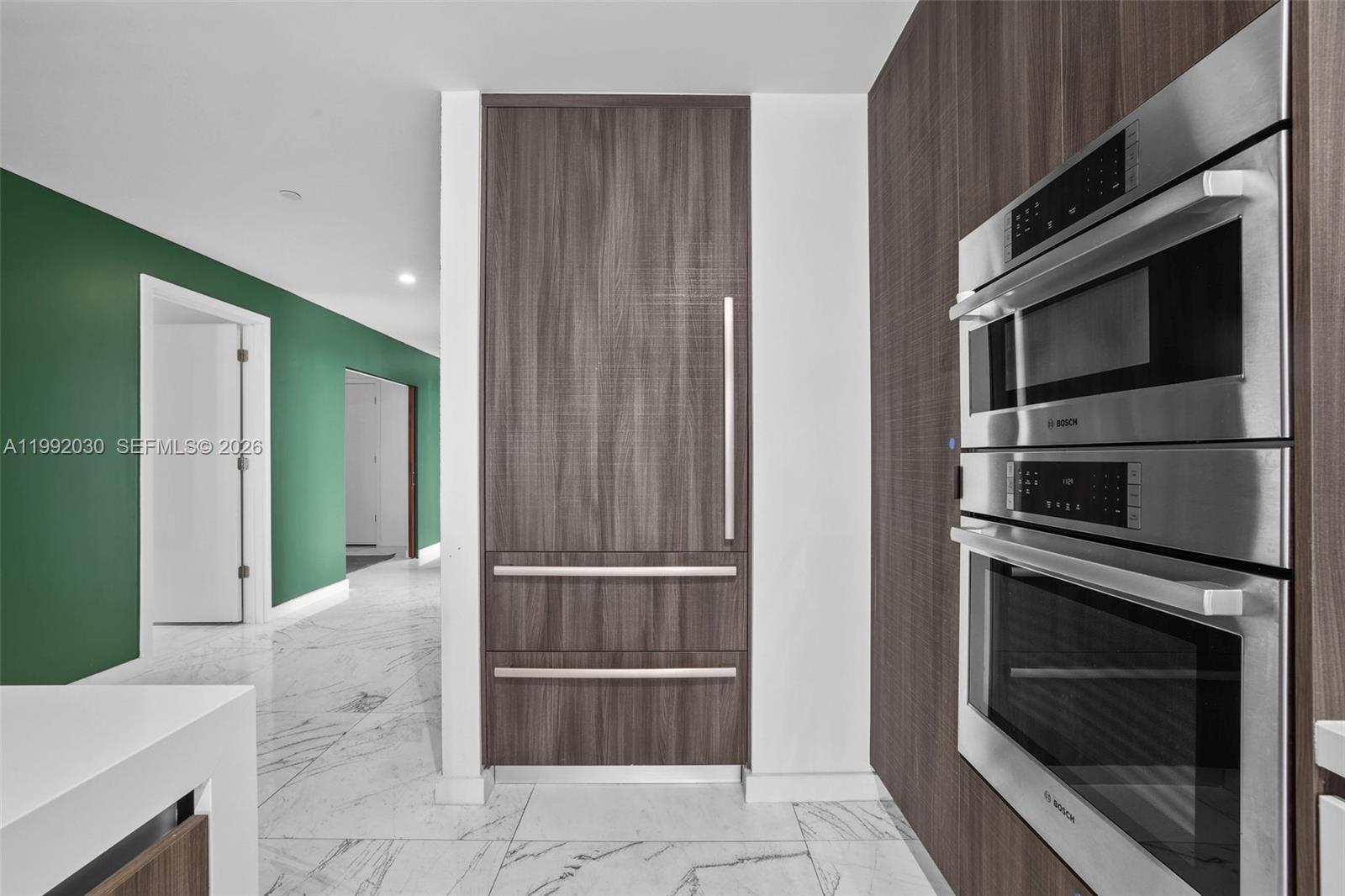 A modern kitchen features wood-paneled cabinetry, stainless steel Bosch appliances, and white marble flooring — 851 NE 1st Ave # 3211, Miami FL 33132, MIAMI, FL