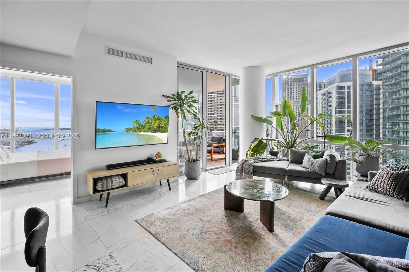 A modern living room features floor-to-ceiling windows, a wall-mounted television, and marble flooring — 851 NE 1st Ave # 3211, Miami FL 33132, MIAMI, FL