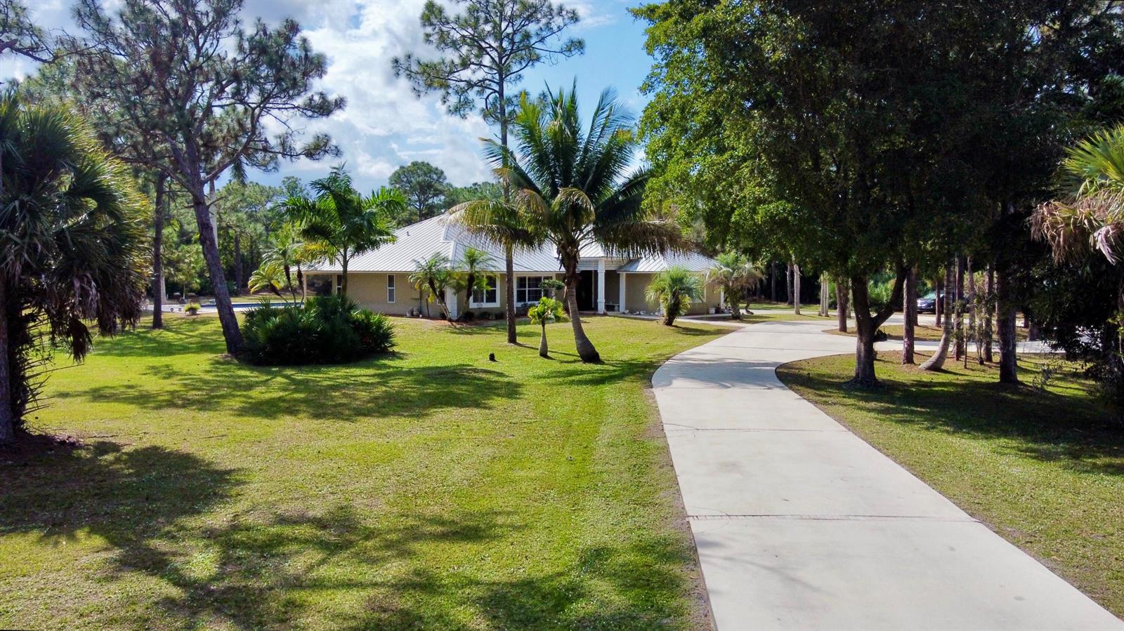 A single-story house with a metal roof sits at the end of a concrete driveway — 2884 SE Ranch Acres Circle, Jupiter FL 33478, JUPITER, FL
