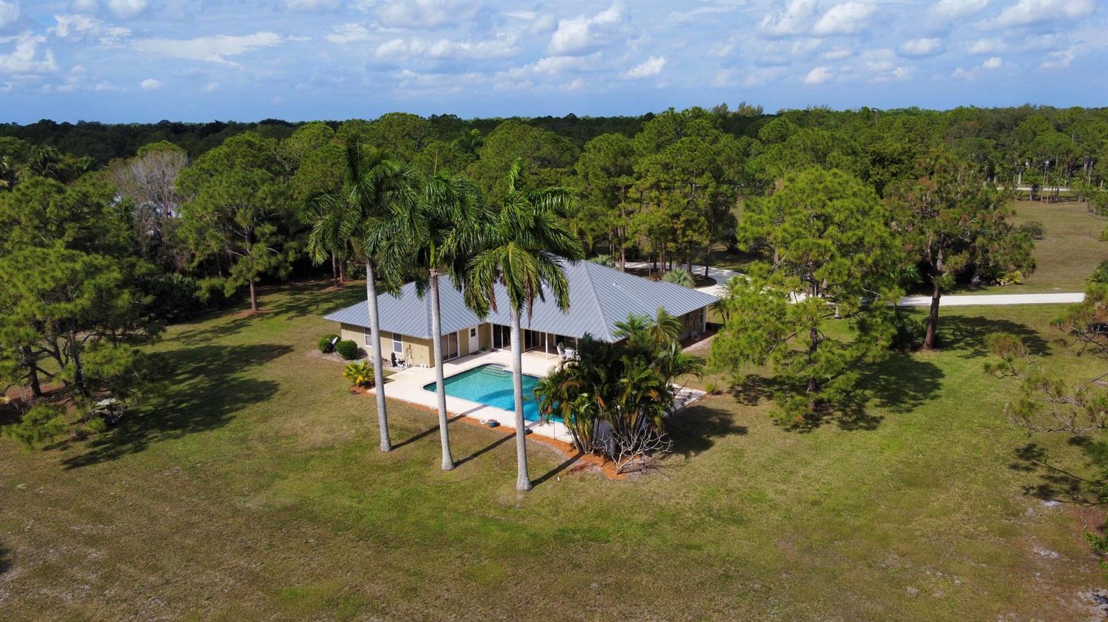 An aerial view of a house with a metal roof, swimming pool, and surrounding trees — 2884 SE Ranch Acres Circle, Jupiter FL 33478, JUPITER, FL