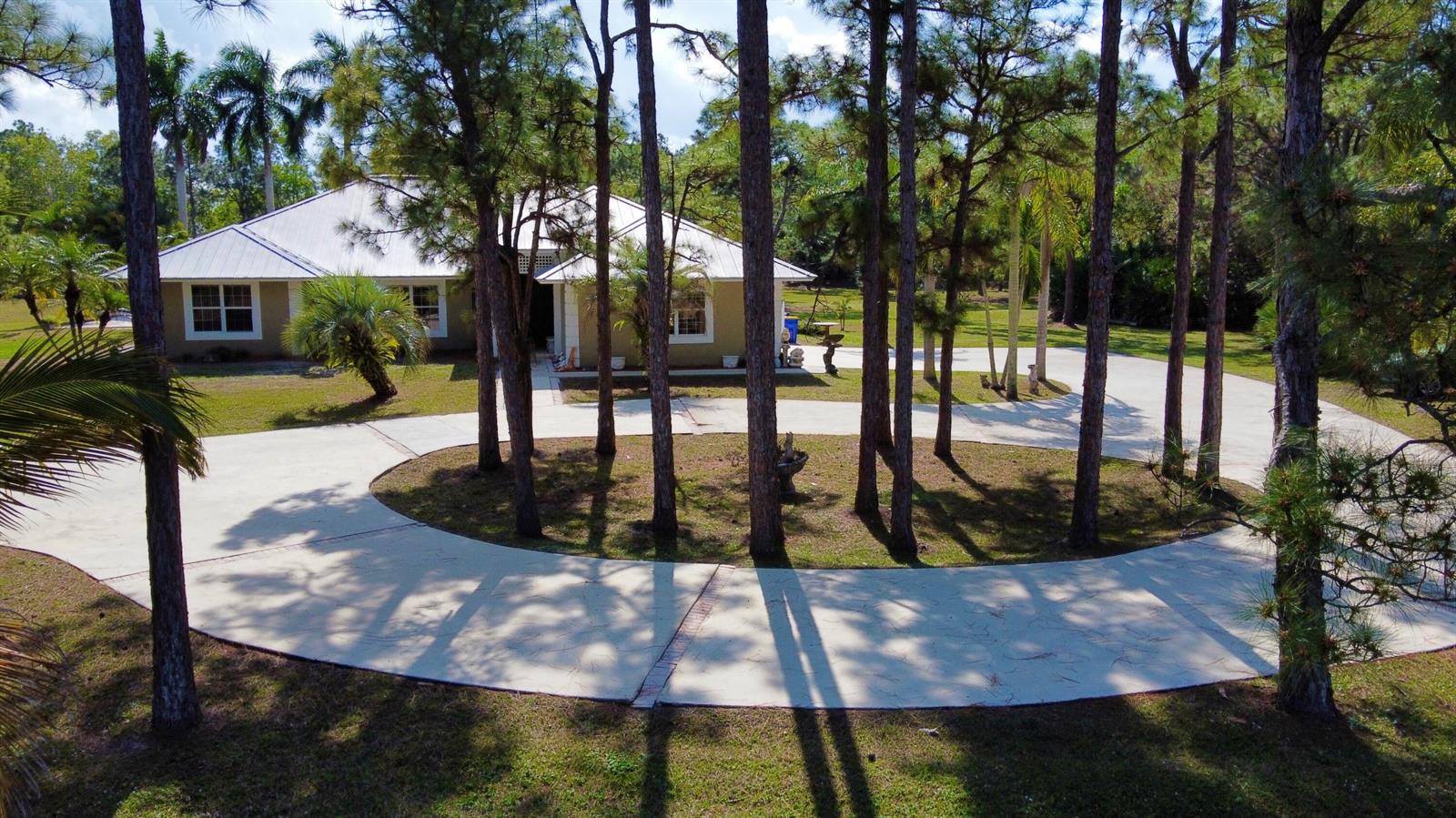 An aerial view shows a house with a metal roof and a circular concrete driveway — 2884 SE Ranch Acres Circle, Jupiter FL 33478, JUPITER, FL