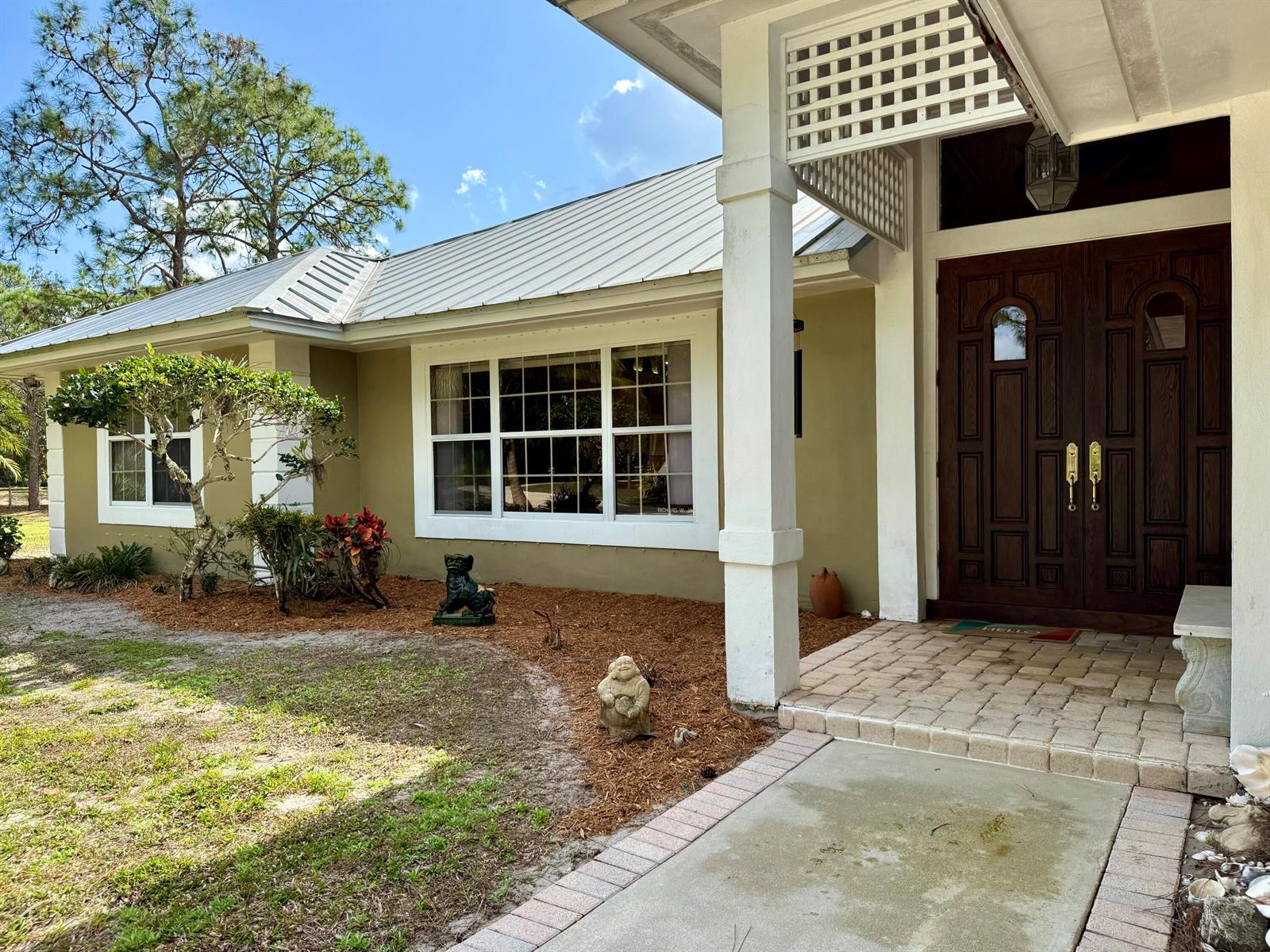 The exterior of a house features a metal roof, tan stucco walls, and a double door — 2884 SE Ranch Acres Circle, Jupiter FL 33478, JUPITER, FL