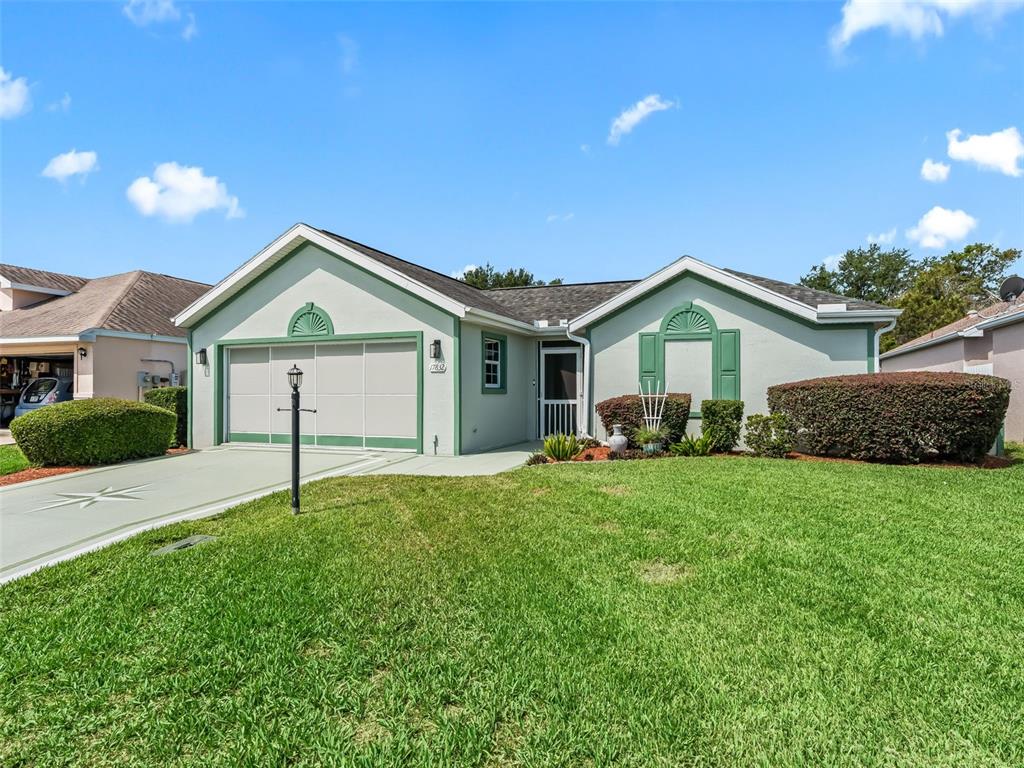 A single-story house with a green-trimmed garage, light-colored stucco, and a front lawn — 17832 SE 115TH COURT, SUMMERFIELD, FL
