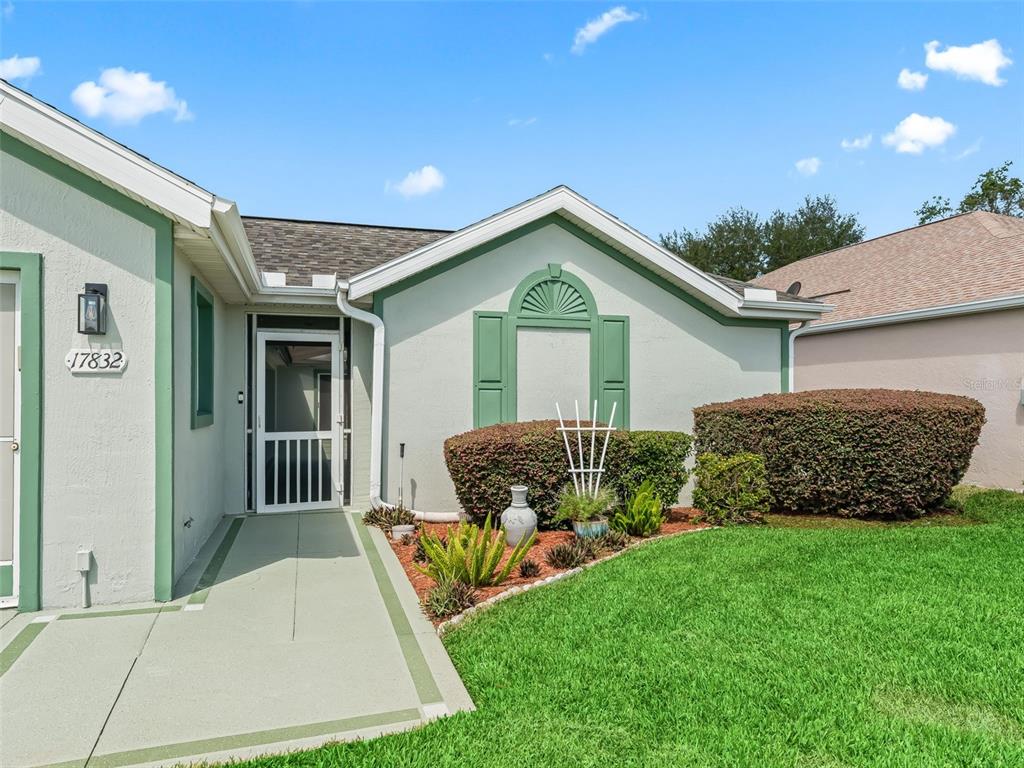 The exterior of a house features a light-colored facade, green trim, and a small garden — 17832 SE 115TH COURT, SUMMERFIELD, FL