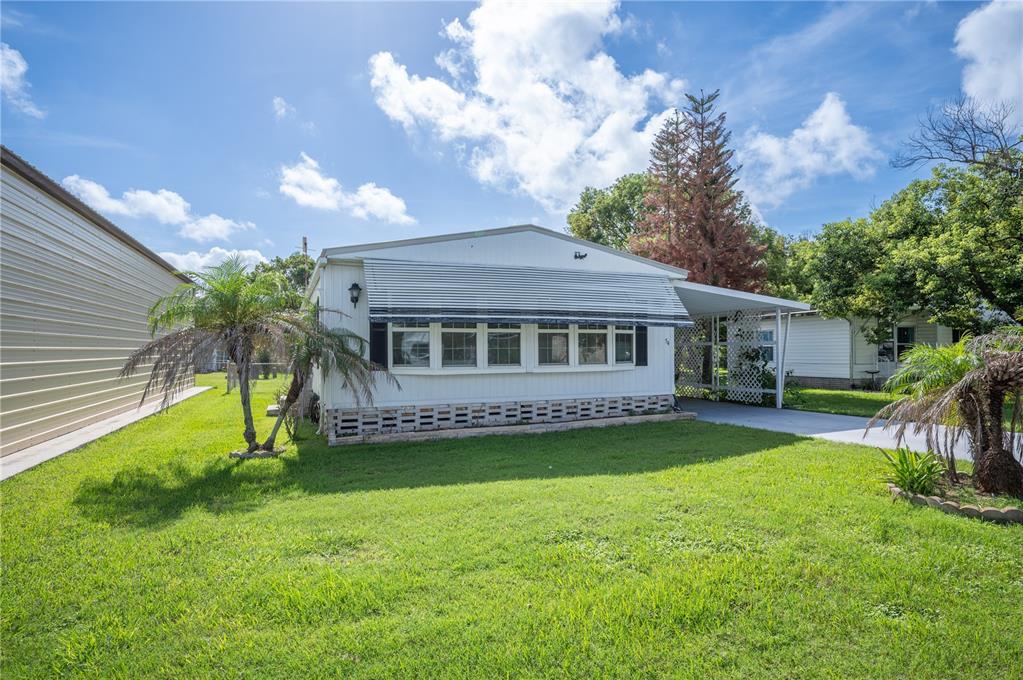 A single-story mobile home with a metal awning, carport, and palm trees on a lawn — 1610 REYNOLDS ROAD UNIT 54, LAKELAND, FL