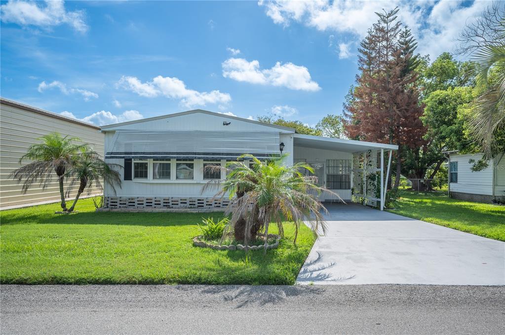 A single-story mobile home with a white exterior, a carport, and a front lawn — 1610 REYNOLDS ROAD UNIT 54, LAKELAND, FL