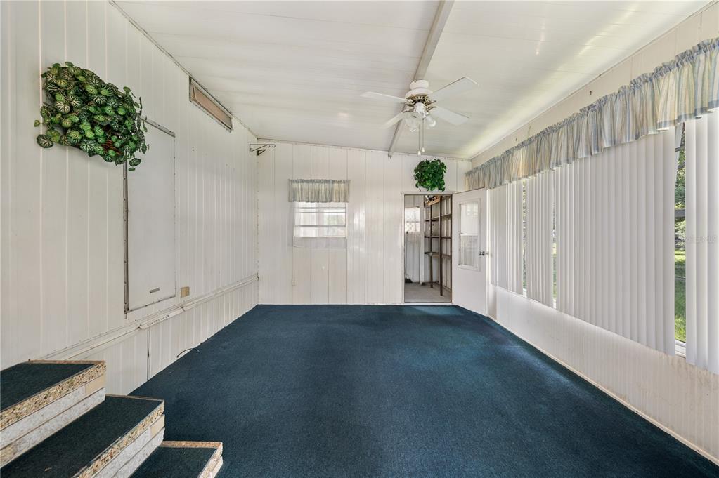 A sunroom with white paneled walls, blue carpeting, a ceiling fan, and vertical window blinds — 1610 REYNOLDS ROAD UNIT 54, LAKELAND, FL