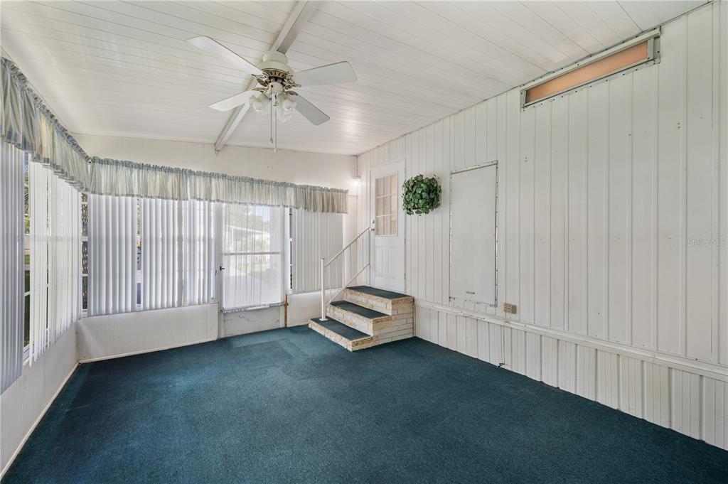 A sunroom features a ceiling fan, green carpeting, white vertical paneling, and stairs leading indoors — 1610 REYNOLDS ROAD UNIT 54, LAKELAND, FL