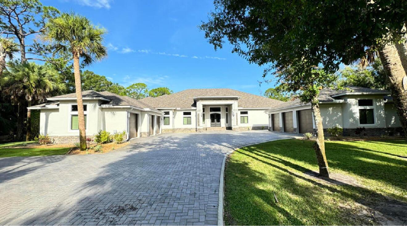 A wide, single-story house with a paved driveway, multiple garage bays, and surrounding palm trees — 145 24th Avenue, Vero Beach FL 32962, VERO BEACH, FL