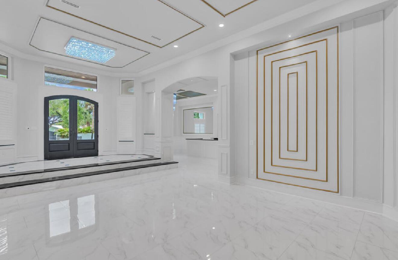 A bright, modern foyer features white marble floors, gold wall trim, and a crystal chandelier — 145 24th Avenue, Vero Beach FL 32962, VERO BEACH, FL