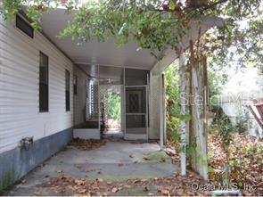 A covered concrete patio leads to a screened-in entryway of a white mobile home — 6980 NE 4TH LANE, OCALA, FL