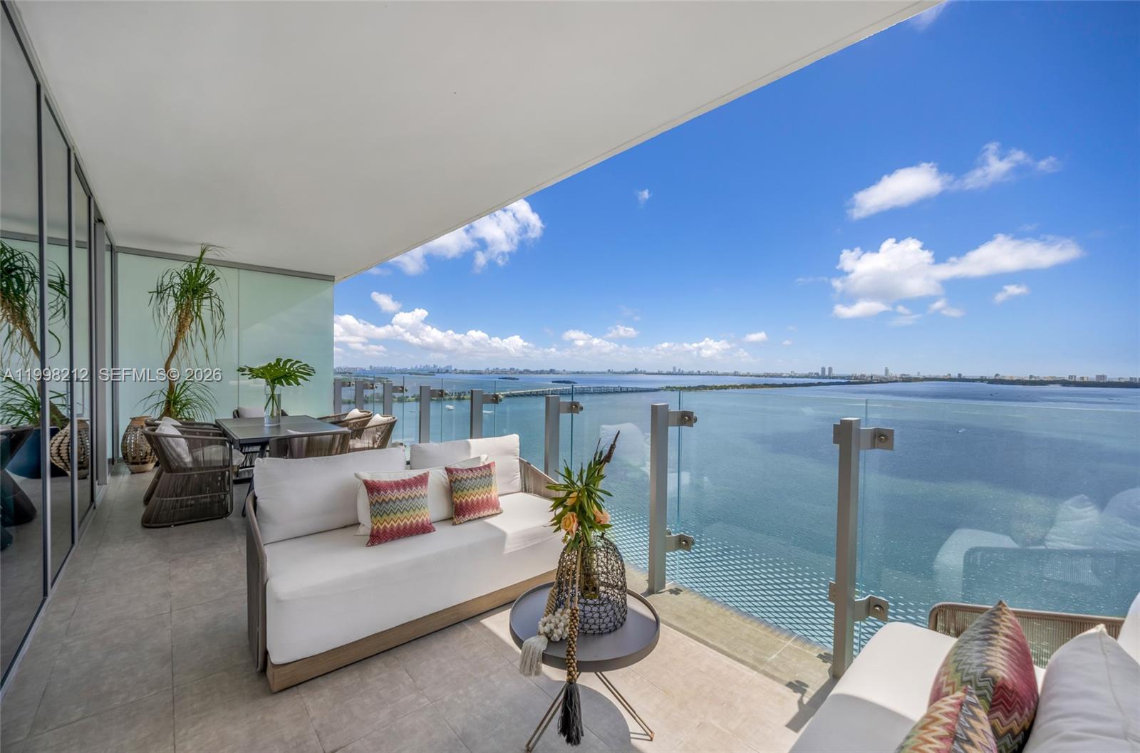A furnished balcony overlooks a large body of water with a distant city skyline — 700 NE 26th Ter # 2202, Miami FL 33137, MIAMI, FL