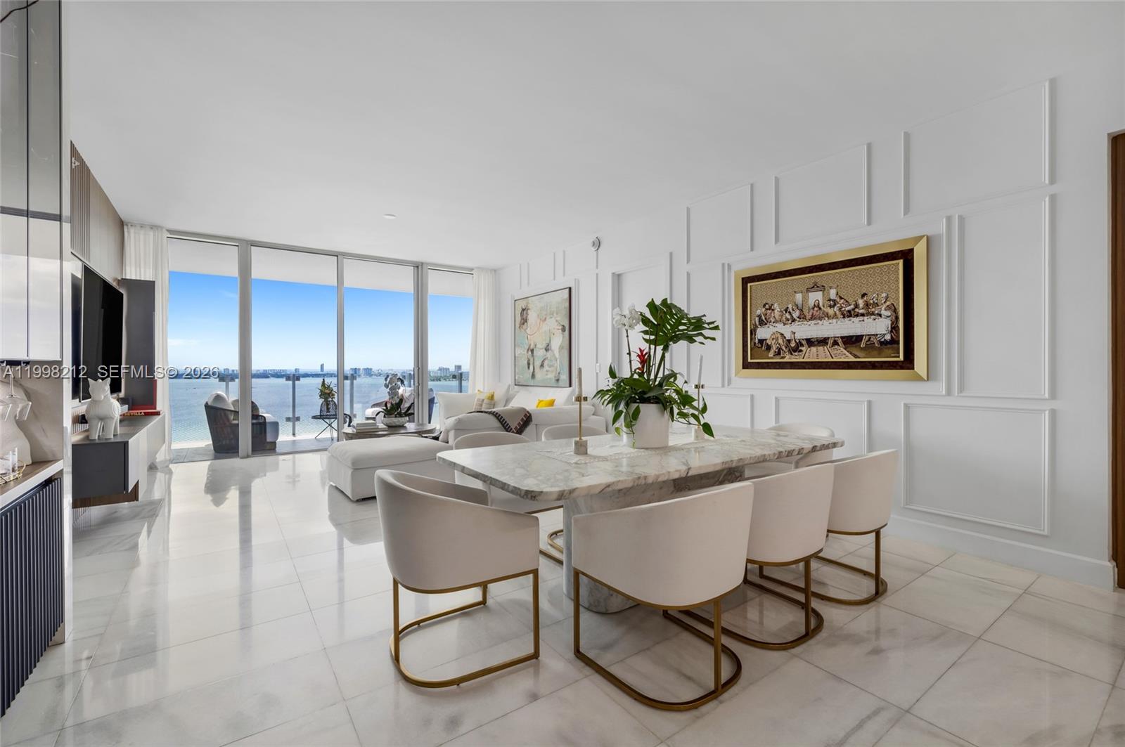 A modern dining room features a marble table, white chairs, and floor-to-ceiling windows overlooking water — 700 NE 26th Ter # 2202, Miami FL 33137, MIAMI, FL