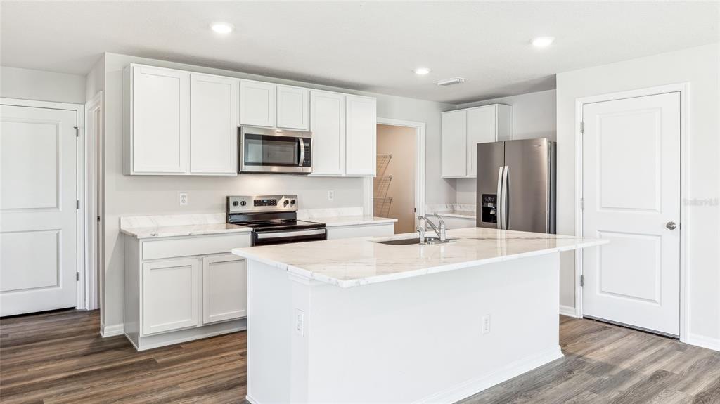 A kitchen with white cabinets, marble-look countertops, a center island, and stainless steel appliances — 9944 MORNING MEADOWLARK TRAIL, PARRISH, FL