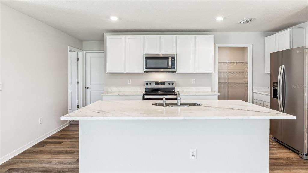 A kitchen features white cabinets, stainless steel appliances, and a large marble-topped island — 9944 MORNING MEADOWLARK TRAIL, PARRISH, FL