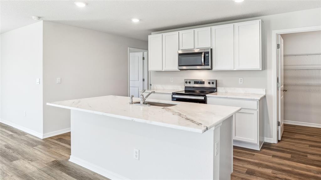 A kitchen features white cabinets, a marble-topped island with a sink, and stainless steel appliances — 9944 MORNING MEADOWLARK TRAIL, PARRISH, FL