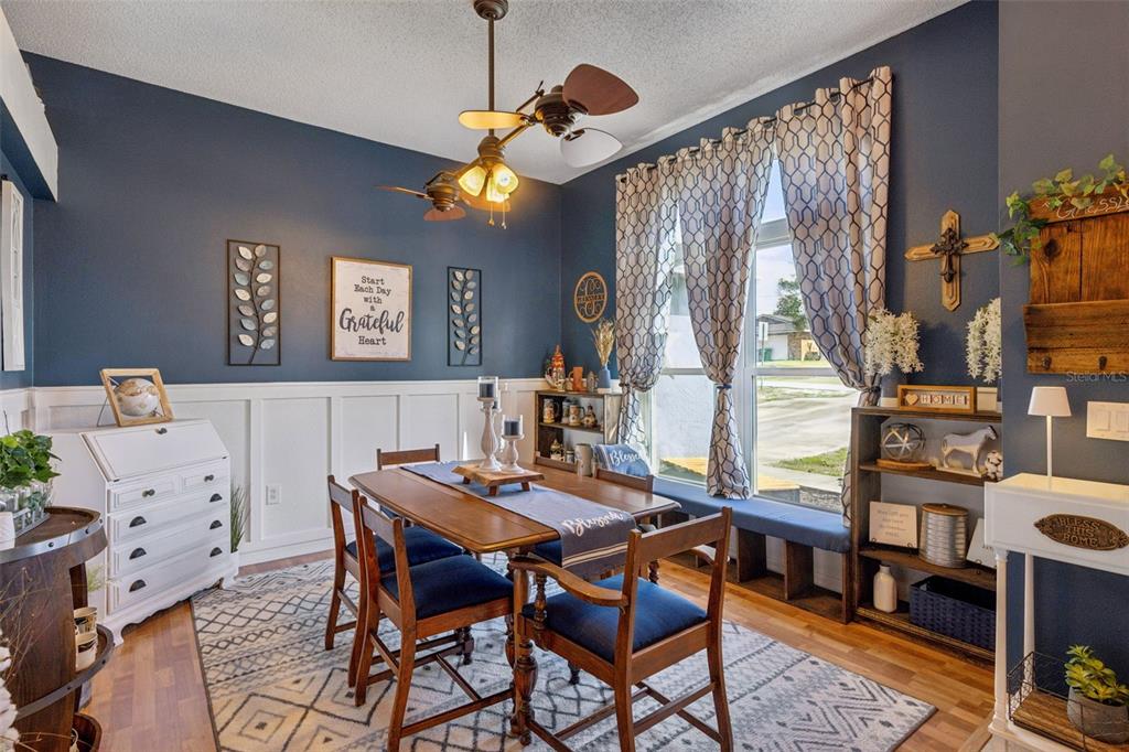 A dining room with blue walls, white wainscoting, a wooden table, and a window seat — 1405 WINTERVILLE STREET, DELTONA, FL
