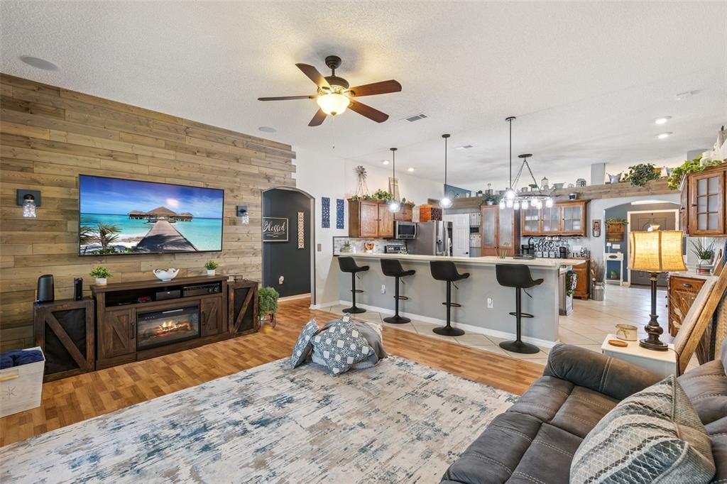 A living room with a wood-paneled accent wall, fireplace console, and an open kitchen island — 1405 WINTERVILLE STREET, DELTONA, FL