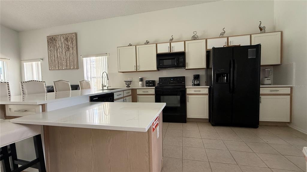 A kitchen features white cabinets, a black refrigerator, and a white-topped island with seating — 513 BAILEY CIRCLE, DAVENPORT, FL