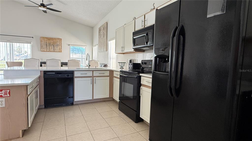 A kitchen features white cabinets, black appliances, and a tiled floor with an adjacent dining area — 513 BAILEY CIRCLE, DAVENPORT, FL
